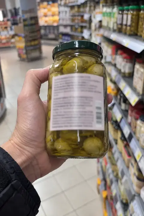 Mano girando un bote en el pasillo del supermercado para leer la etiqueta